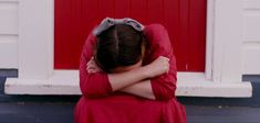 a woman sitting in front of a red door with her head resting on her hands