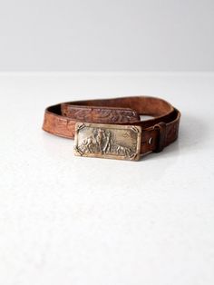 This is a vintage tooled leather belt with brass buckle.  The saddle brown leather belt has a classic western floral pattern.  A removable brass buckle pictures a cowboy with his horse and calf. CONDITIONIn good condition with wear consistent with age and use. MARKED SIZE:  30FITS: 29" - 32.5"MEASUREMENTSStrap Length:  34.5"  ..  87.6 cmStrap Width:  1"  .. 2.54 cmBuckle:  2.75" x 1.375"  ..  7 cm x 3.5 cm121941 Vintage Adjustable Belt Buckles For Ranch, Vintage Brown Belt For Western-themed Events, Vintage Adjustable Belts And Suspenders With Brass Buckle, Vintage Brown Belt Buckles With Brass Buckle, Vintage Leather Belts For Ranch, Vintage Engraved Leather Belt, Vintage Adjustable Belt For Western-themed Events, Vintage Adjustable Belt Buckles For Western-themed Events, Vintage Adjustable Belt With Brass Buckle