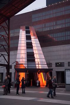 people are walking around in front of a building with an orange light coming from it