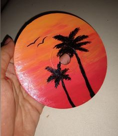 a hand holding a painted disc with palm trees