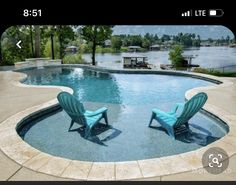 two lawn chairs sitting in the middle of a swimming pool next to a large body of water