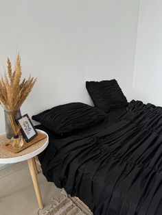 a black comforter on a bed next to a table with a vase and dried plant