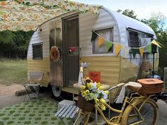 a yellow bicycle is parked next to an old camper with flowers on the front