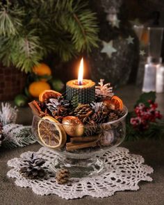 a candle is lit in a glass bowl filled with pine cones, oranges and other decorations