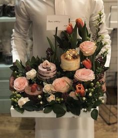 a man is holding a bouquet of flowers and cakes in front of his face while wearing a white shirt