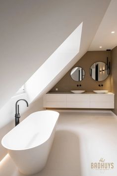 a white bath tub sitting under a bathroom window next to a sink and two mirrors