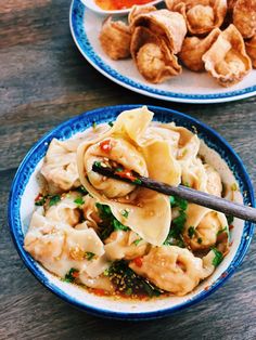 two plates filled with dumplings and vegetables on top of a wooden table next to dipping sauce