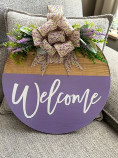 a welcome sign with purple flowers and greenery on the back of a gray chair