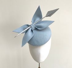 A truly elegant baby pale blue felt bow cocktail hat with silver detailing. The perfect choice for Royal Ascot, a winter wedding or special occasion. Made in a stunning shade of pale blue wool felt, this circular percher style cocktail hat features a double bow in matching pale blue felt that sits neatly to one side. Wrapped within the bows is a silver arrow head quill which gives this headpiece a statement striking look. Measuring 16cm, it is fitted with a fine elastic in a colour that would bl Affordable Blue Fun Hats, Luxury Blue Mini Hats For Evening, Blue Curved Brim Felt Hat For Party, Chic Blue Fascinator For Races, Blue Felt Hat With Curved Brim For Party, Blue Curved Brim Felt Hat For Parties, Luxury Blue Fascinator For Spring, Elegant Light Blue Fascinator For Wedding, Elegant Light Blue Party Fascinator