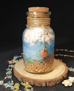 a glass jar filled with sand and sea shells on top of a wooden stand next to beads