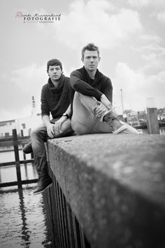 two young men sitting next to each other on a pier