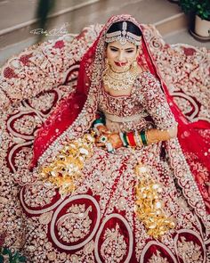 a woman in a red and gold bridal outfit sitting on a rug with jewelry