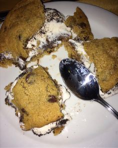 a white plate topped with ice cream and chocolate chip cookie desserts next to a spoon