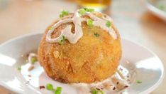 a fried food item on a white plate with green onions and mayonnaise drizzled over it