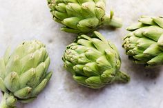 three green artichokes sitting next to each other on a white counter top