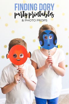 two children with masks on their faces holding up orange and blue paper fish shaped props