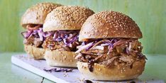 three pulled pork sandwiches sitting on top of a cutting board