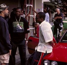 a group of men standing around a red car