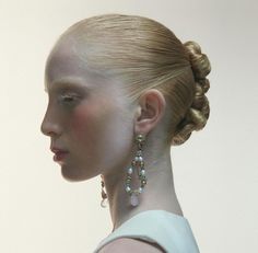 a woman with blonde hair wearing earrings and a white dress is looking off to the side