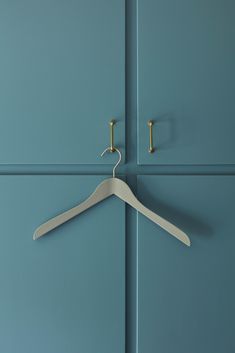 a white hanger is hanging on a blue wall with two gold hooks in front of it