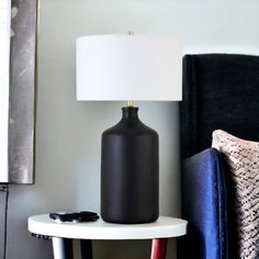 a black lamp sitting on top of a white table next to a blue chair and pillow