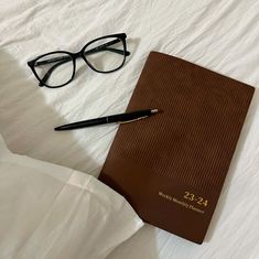 a book, pen and glasses on a bed