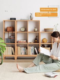 a woman sitting on the floor reading a book in front of a bookshelf