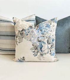 three pillows with blue and white flowers are on a table next to each other in front of a white wall