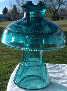 a blue glass vase sitting on top of a white table cloth in the middle of a field