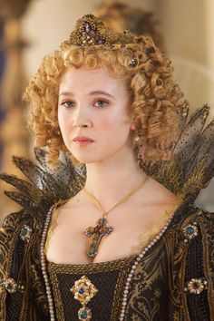 a woman with curly hair wearing a black dress and tiara, looking at the camera