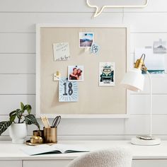 a white desk topped with a lamp next to a wall mounted calendar and other items