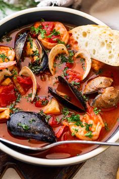 a white bowl filled with seafood and mussels next to bread on a wooden table