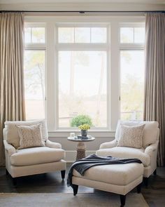 a living room with two white chairs and a table in front of a large window