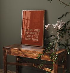 a wooden table topped with a vase filled with white flowers next to a framed poster