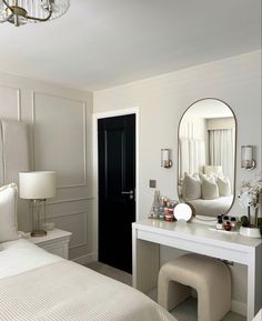 a bedroom with a white bed, mirror and dressing table in front of the door