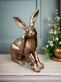 a golden rabbit statue sitting on top of a table next to a vase with flowers