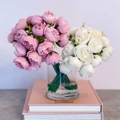 two vases filled with white and pink flowers sitting on top of a stack of books