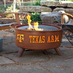 a fire pit sitting on top of a stone floor next to chairs and trees in the background