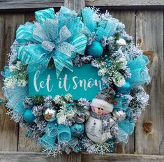 a snowman wreath with blue and silver decorations hanging on a wooden door that says let it snow