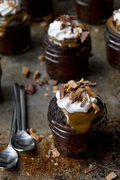 two jars filled with dessert sitting on top of a table next to silver spoons