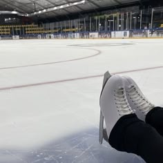 someone is sitting on the ice with their feet propped up in front of an empty hockey rink