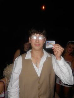 a man wearing glasses holding up a card in front of his face and people behind him