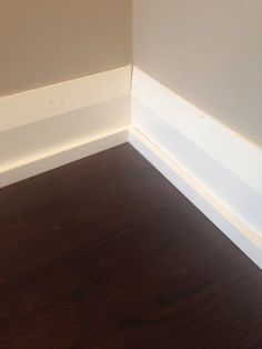 the corner of a room with wood flooring and white painted trim on the walls