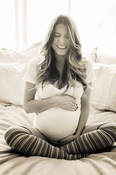 a pregnant woman sitting on top of a bed with her belly tucked under her stomach