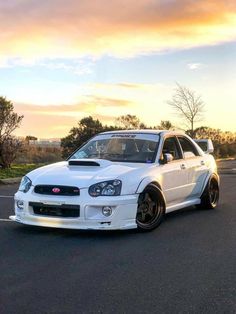 a white subarunt parked in a parking lot with the sun setting behind it