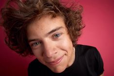 a close up of a person wearing a black shirt with curly hair and blue eyes