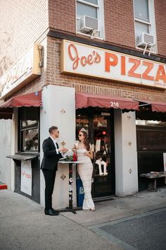 a man and woman standing in front of a pizza shop