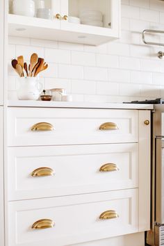 a kitchen with white cabinets and gold pulls on the drawers, including utensils