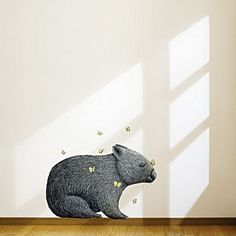 a bear sitting on the floor in front of a wall with butterflies coming out of it