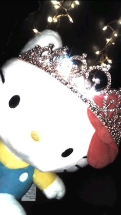 a hello kitty stuffed animal with a crown on it's head and lights in the background